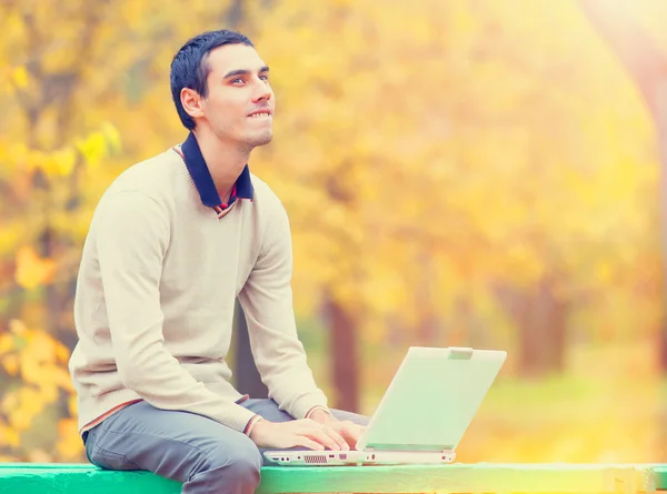 Programmeur met laptop zitten in herfst park — Stockfoto