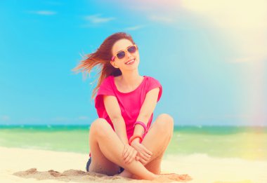 Funny teen girl sitting on the sand at the beach. clipart