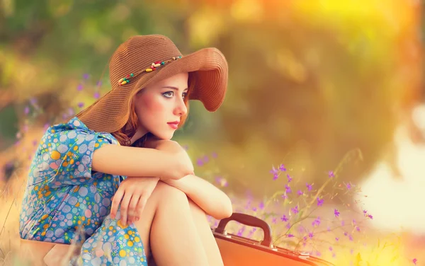 秋の草で座っているスーツケースの赤毛の女の子 — ストック写真