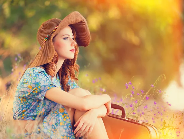 Roodharige meisje met koffer zittend op herfst gras — Stockfoto