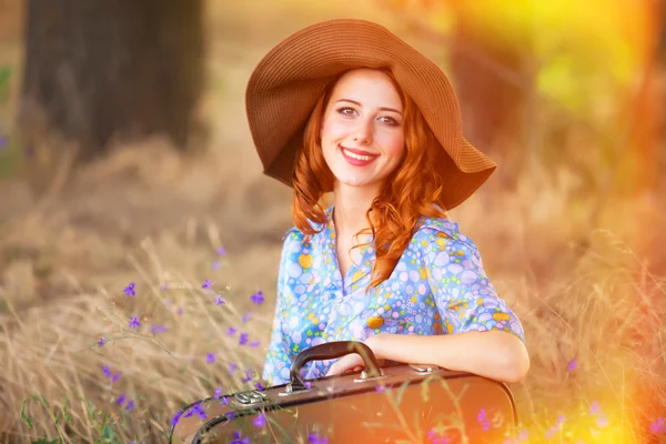 Ragazza rossa con valigia seduta all'erba autunnale — Foto Stock