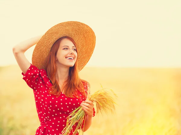 Руда дівчина в червоній сукні на пшеничному полі — стокове фото