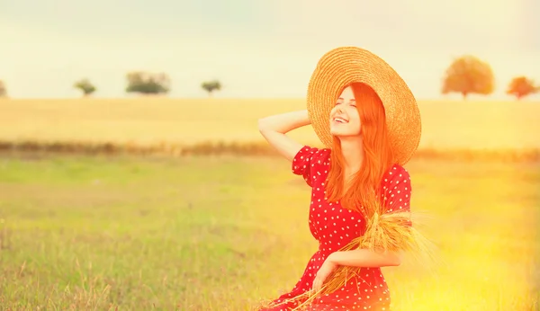 Руда дівчина в червоній сукні на пшеничному полі — стокове фото