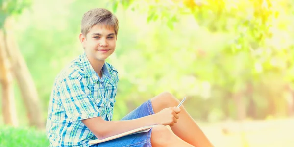 Tiener jongen met boeken en notebook in het park. — Stockfoto