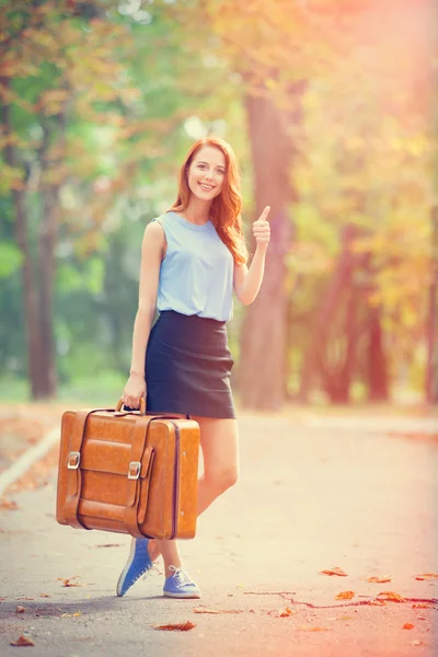 Chica pelirroja feliz con maleta en el parque de otoño . — Foto de Stock