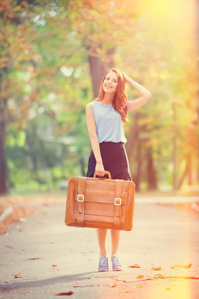 Chica pelirroja feliz con maleta en el parque de otoño . — Foto de Stock