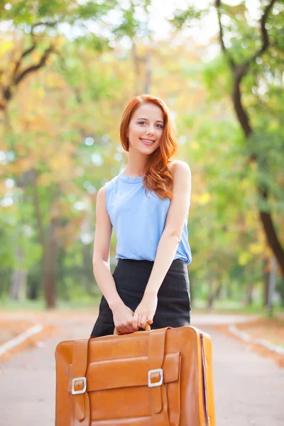 Gelukkig roodharige meisje met koffer in de herfst park. — Stockfoto