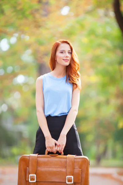 Happy redhead girl with suitcase in the autumn park. — Stock Photo, Image