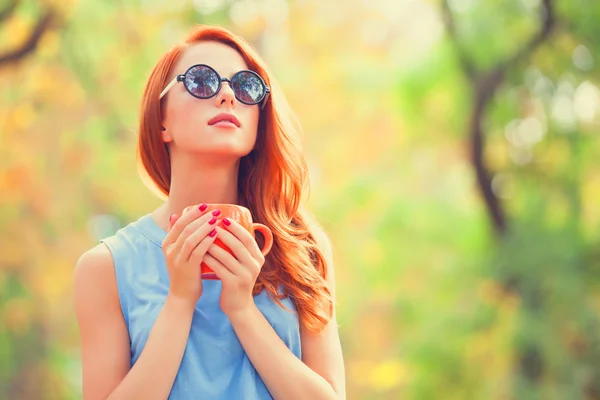 Successful redhead girl winh cup in the autumn park. — Stock Photo, Image