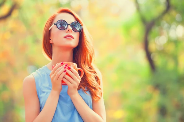 Éxito chica pelirroja winh taza en el otoño parque . — Foto de Stock