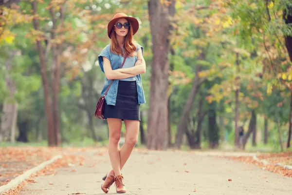 Kızıl saçlı kız güneş gözlüğü ve şapka sonbahar Park. — Stok fotoğraf