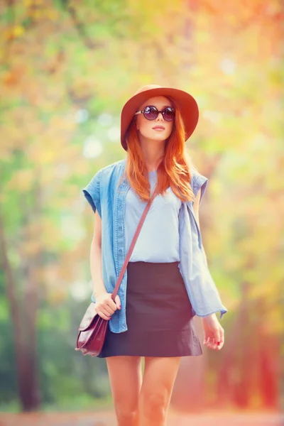 Rothaarige Mädchen mit Sonnenbrille und Hut im Herbstpark. — Stockfoto