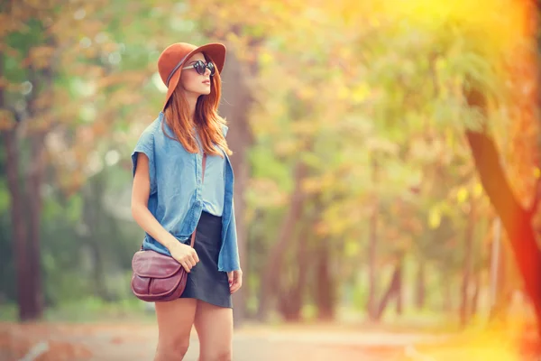 Rothaarige Mädchen mit Sonnenbrille und Hut im Herbstpark. — Stockfoto