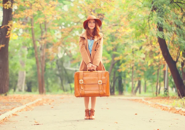 Roodharige meisje met koffer in de herfst park. — Stockfoto