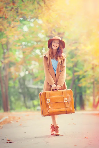 Ragazza rossa con valigia nel parco autunnale . — Foto Stock