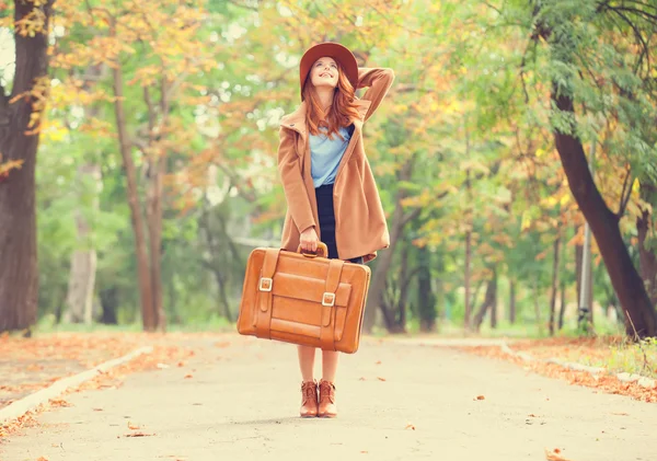 Ragazza rossa con valigia nel parco autunnale . — Foto Stock