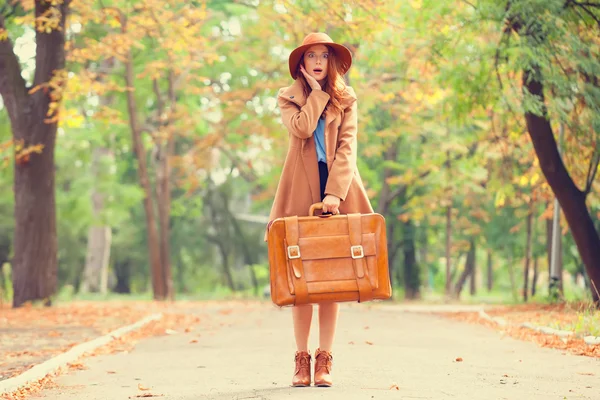 Redhead girl with suitcase in the autumn park. — Stock Photo, Image