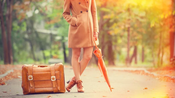 Gril in coat with umbrella and suitcase in the park. — Stock Photo, Image