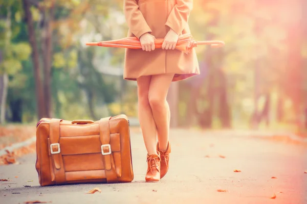 Gril in jas met paraplu en koffer in het park. — Stockfoto