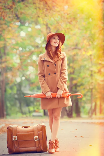 Ragazza rossa con ombrello e valigia nel parco autunnale . — Foto Stock