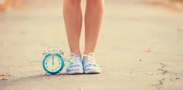 Teenager's foots and alarm clock in gumshoes in the park. — Stock Photo, Image