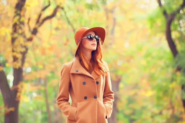 Roodharige meisje in zonnebril en hoed in de herfst park. — Stockfoto