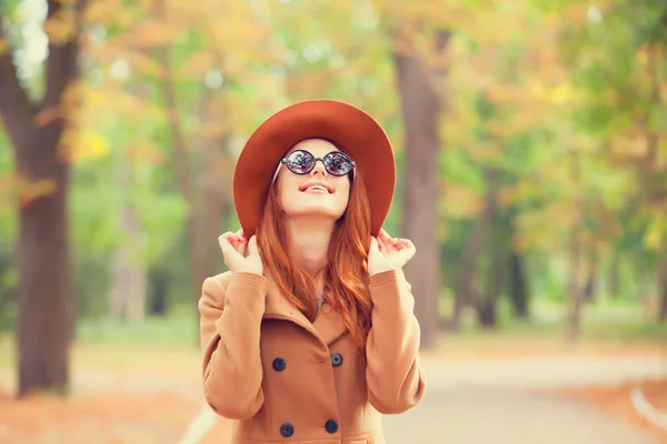 Roodharige meisje in zonnebril en hoed in de herfst park. — Stockfoto