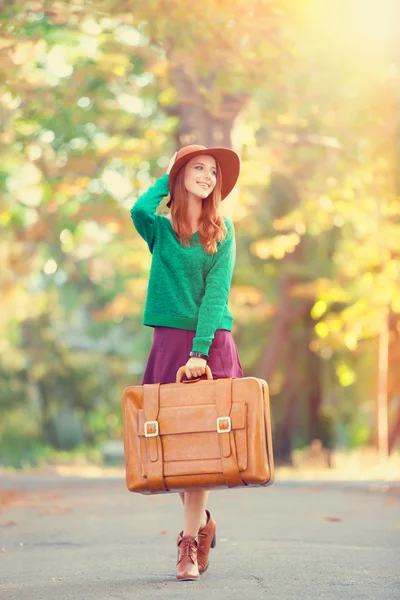 Schöne rothaarige Mädchen mit Koffer im Park. — Stockfoto