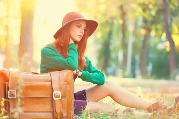 Beautiful redhead girl with suitcase in the park. — Stock Photo, Image
