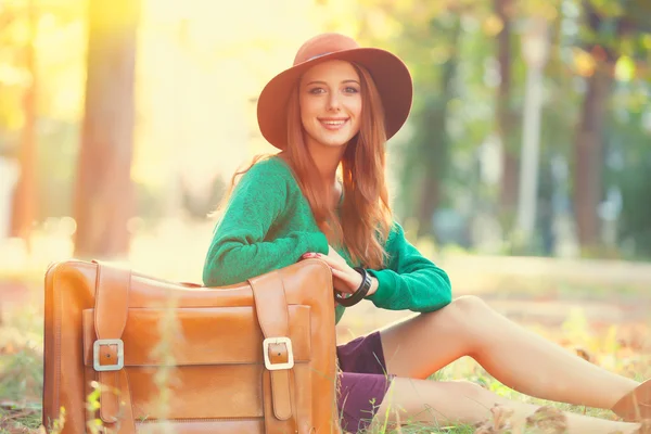 Mooi roodharig meisje met koffer in het park. — Stockfoto
