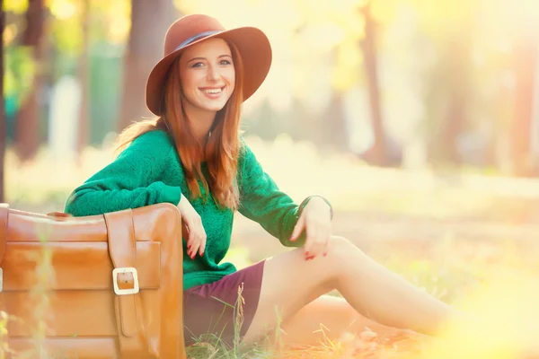 Όμορφη κοκκινομάλλα κοπέλα με βαλίτσα στο πάρκο. — Φωτογραφία Αρχείου