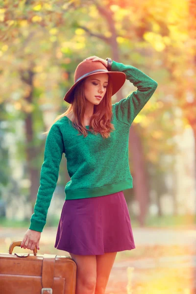 Красивая рыжая девушка с чемоданом в парке . — стоковое фото