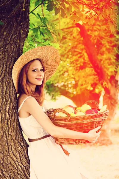 Schöne rothaarige Mädchen mit Früchten im Korb im Garten. — Stockfoto