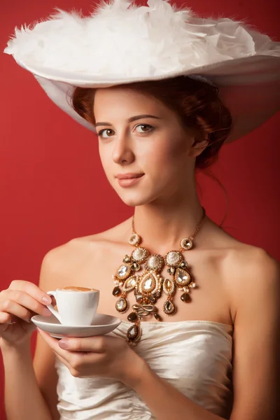 Portret van de roodharige Edwardiaanse vrouw met cup op rode achtergrond. — Stockfoto