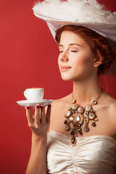 Portrait of redhead edwardian women with cup on red background. — Stock Photo, Image