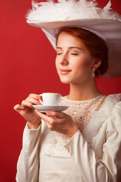 Portret van de roodharige Edwardiaanse vrouw met cup op rode achtergrond. — Stockfoto