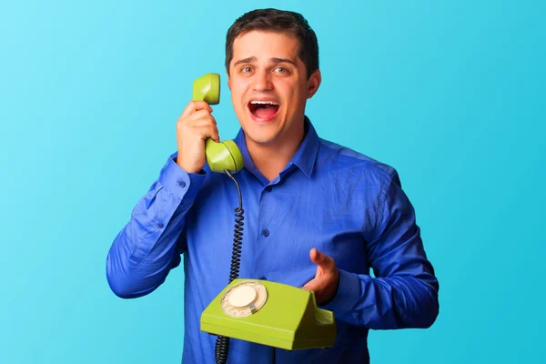 Hombre sorprendido en camisa con teléfono sobre fondo azul . — Foto de Stock