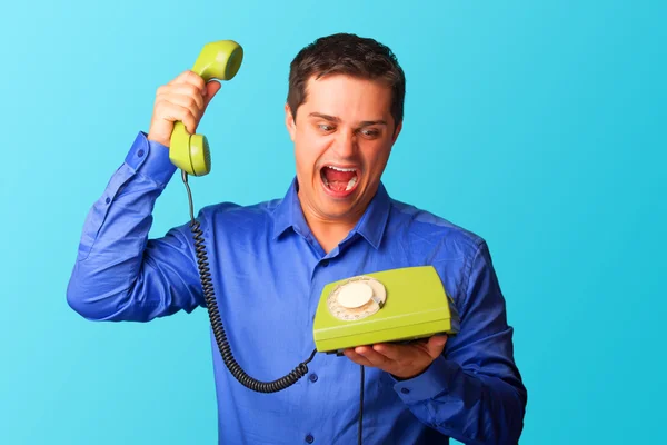 Verrast man in shirt met telefoon op blauwe achtergrond. — Stockfoto