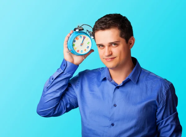 Hombre casual en camisa con despertador sobre fondo azul . — Foto de Stock