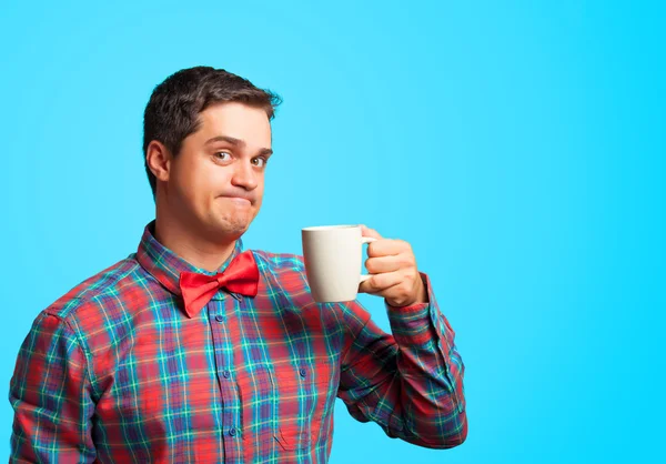 Verrast man in shirt met cup op blauwe achtergrond. — Stockfoto