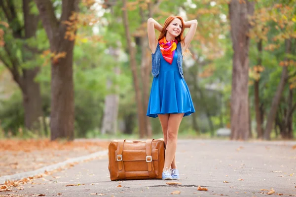 Mooi roodharig meisje met koffer in het park. — Stockfoto