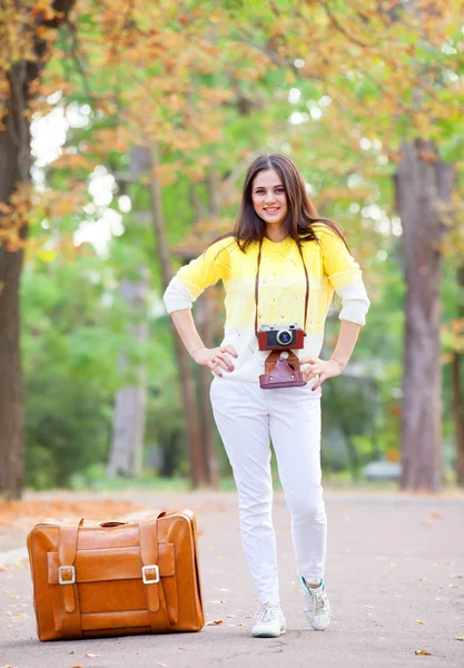 Krásná brunetka s kufrem v parku. — Stock fotografie