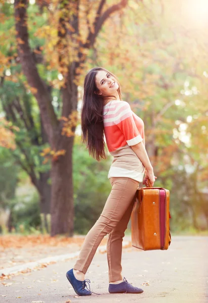 Mooie brunette meisje met koffer in het park. — Stockfoto