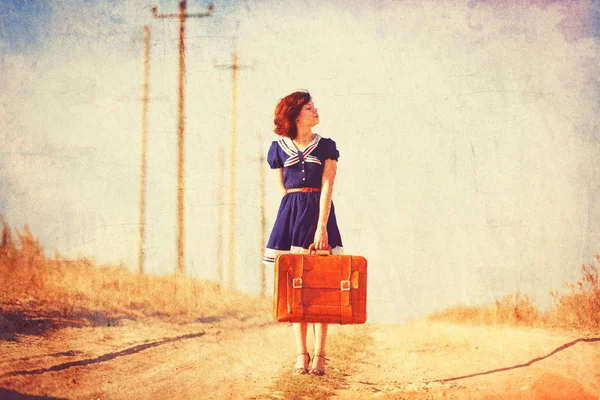 Piękna brunetka dziewczyna z walizką na drodze wsi. — Zdjęcie stockowe