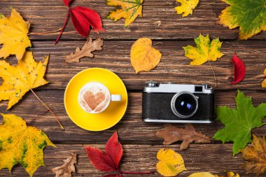 Sonbaharda yapraklar, ahşap masa üstünde fotoğraf makinesi ve kahve Kupası.