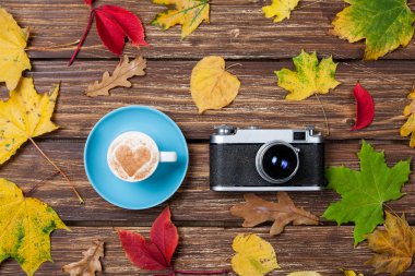 Sonbaharda yapraklar, ahşap masa üstünde fotoğraf makinesi ve kahve Kupası.