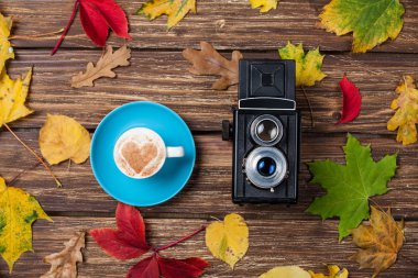 Sonbaharda yapraklar, ahşap masa üstünde fotoğraf makinesi ve kahve Kupası.