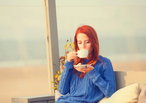 Rödhårig tjej med kopp sitter i café nära havskust. — Stockfoto