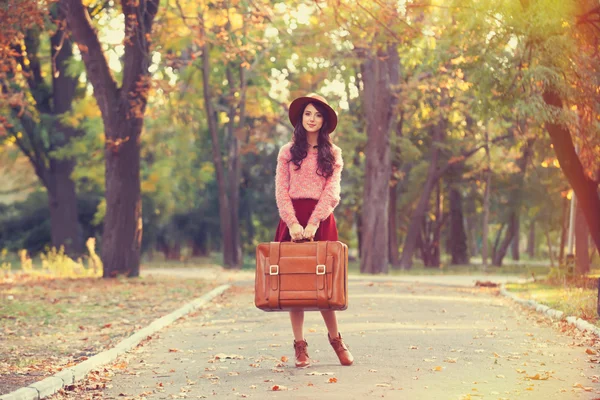 Krásná brunetka s kufrem v parku. — Stock fotografie