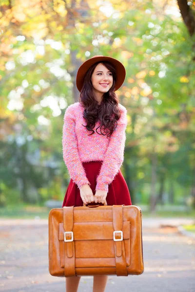 Krásná brunetka s kufrem v parku. — Stock fotografie